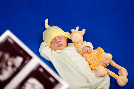 Sweet newborn sleeping on a blue blanket. Sweet boy in pajamas taking a nap with toy giraffe....