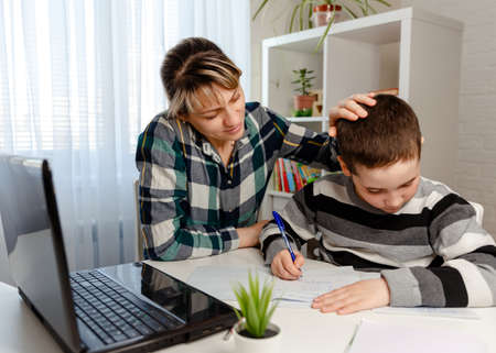 Child doing homework with books, textbooks. Mother helping her son making school homework at home. Home schooling and concept of COVID-19 pandemic infectionの写真素材