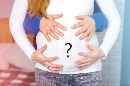 Pregnant couple of husband and wife feels love and relax at home. Young expecting woman holds baby in pregnant belly. Father take care of pregnant mother. Concept of maternity and pregnancy care.の写真素材