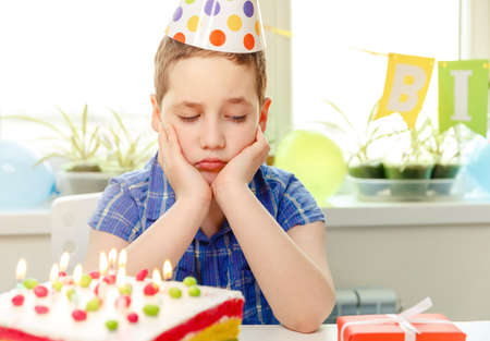 Sad child crying at birthday party. Festive colorful background with cake and balloons. Birthday...