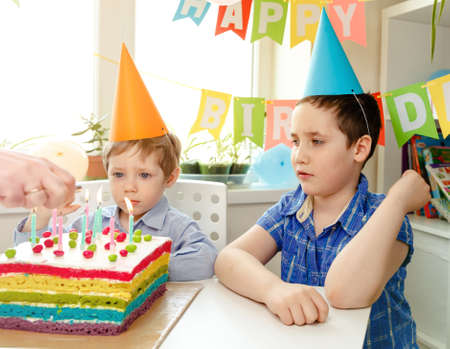 Beautiful kids, little boys celebrating birthday and blowing candles on homemade baked cake, indoor....