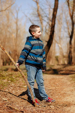Funny child playing with a stick in the spring forest in the fresh air. Concept of family recreation and active lifestyleの写真素材