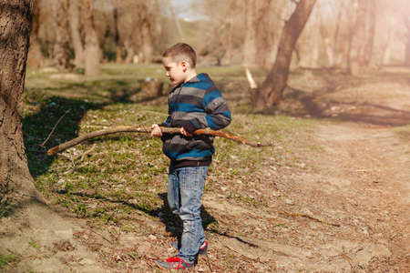 Cute child with a stick on top of a hill playing war games in the spring forest in the fresh air....
