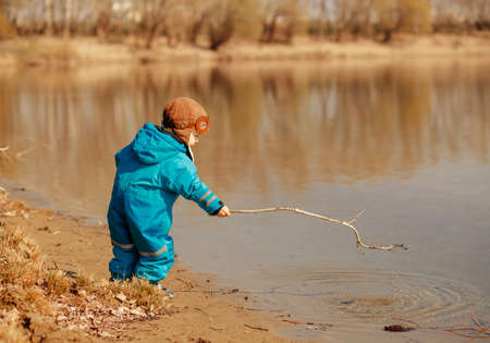 A wonderful baby is playing on the Bank of the river in the open air. Concept of family recreation and active lifestyleの写真素材