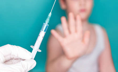 Hand of boy handing stop hand to doctor and refuse vaccination isolated on turquoise background. Doctor Vaccinates Child. Afraid if vaccination. Vaccination of children concept, preventionの写真素材