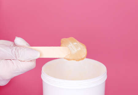 Close-up hands of cosmetologist in white gloves holding paste for sugaring depilation on pink background. Copy space. Depilation and beauty conceptの写真素材