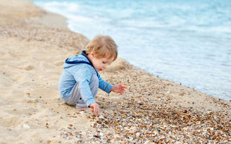 Beautiful child boy playing with sand and running in the water on sunset. Boy throwing rocks....