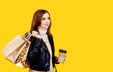 Young girl isolated on yellow background. Happy woman hold shopping package bags with purchases and...