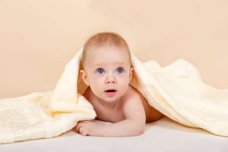Cute baby boy wearing diaper and yellow towel in the bedroom. Newborn child relaxing in bed after...