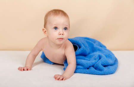 Child boy wearing diaper and blue towel after bath or shower on the bed. Clean dry kid. Textile for infants. Bathing and washing of little kids. Children hygiene. Baby caring, family life, childhoodの写真素材