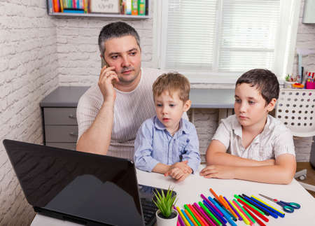 Young busy father trying to work at home with children. Work from home. Freelancer is working on...