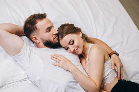 Beautiful loving couple kissing in bed. Young happy family lying together on white background....