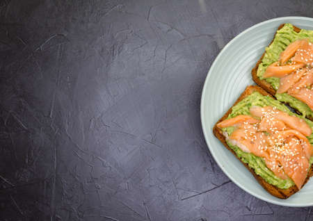 Two delicious toast with rye bread, avocado, smoked salmon on dark concrete background. Homemade sandwich with trout, guacamole. Danish open sandwiches. Healthy food, tasty breakfast. Copyspaceの写真素材