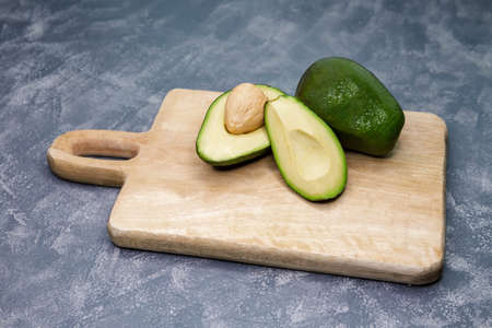 Ripe avocado cut in half on old wooden table. Food background with fresh whole and sliced avocado on...