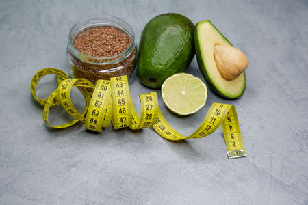 Raw avocado with measuring tape on grey background. Healthy balanced diet concept, weight loss,...