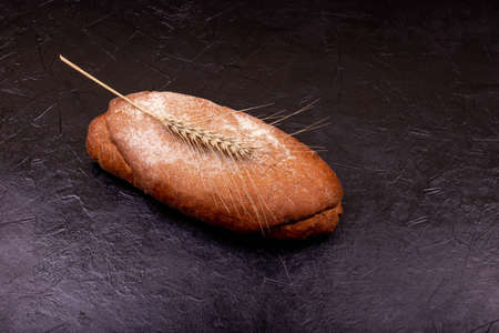 Handmade loaf on stone black surface. Freshly baked homemade bread. Rustic sourdough bread with crispy crust. Rye bread on dark background. Brown loaf of whole grain bread and shocks of wheat.の写真素材
