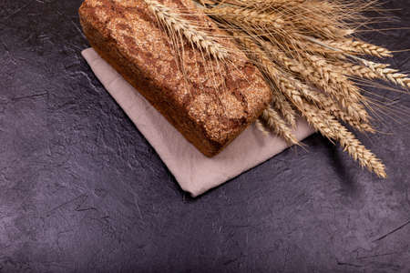 Rustic sourdough bread with crispy crust. Rye bread on dark background. Loaf of whole grain bread and shocks of wheat. Freshly baked homemade bread. Cropped view of brown loaf on stone black surface.の写真素材