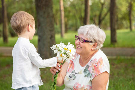 Beautiful boy giving a flower to grandma. Happy mothers day. Grandson and grandmother spending time...