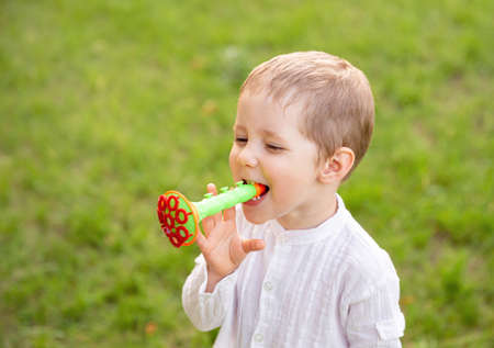 Happy little kid blowing soap bubble in school garden. Caucasian child playing with soap bubbles....
