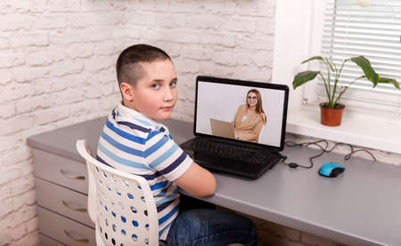 Boy student video conference e-learning with teacher and classmates on computer in living room....