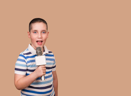 Singing child holds microphone in his hands on the same level with his opened mouth. Young boy is...