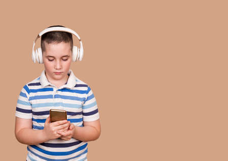 Happy little child listening music with headphones. Cheerful young boy listening to the music in headphones and mobile phone. Smiling boy using smartphone and listening music. Overstimulated children.の写真素材