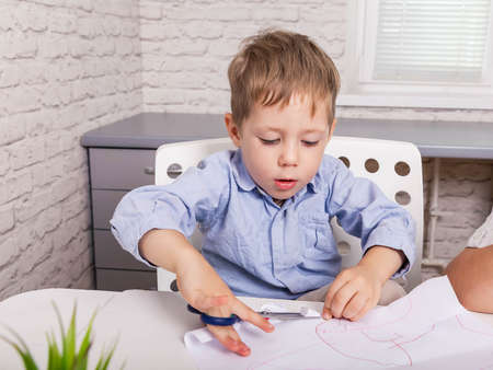 Craft for children. Kid cutting with scissors and gluing paper. Little happy boy play with paper....