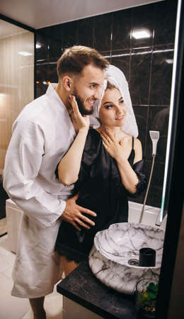 Husband and wife in the bathroom fooling around in front of the mirror. Beautiful young couple having fun. Happy couple take a shower together and enjoy. Iintimate couple is spending nice time at homeの写真素材