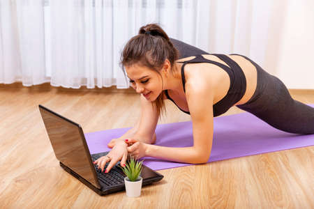 Attractive young woman doing yoga and stretching online at home. Fit woman doing yoga and watching...