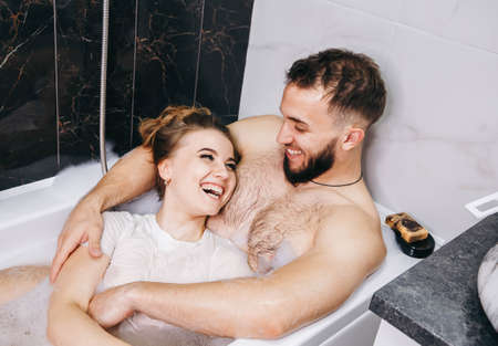 Couple kissing in bathtub. Intimate couple is spending nice time at home. The loving pleasures of a married couple in the bathroom. Young passionate couple hugging. Lovers enjoying time togetherの写真素材