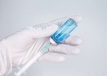 Gloved hand holding a syringe. Coronavirus, Covid 19 virus, vaccine vial. A hand holding syringe in...