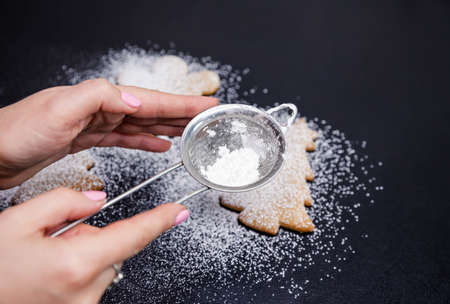 Step 6 of 6. Powdered sugar scattered on a black stone countertop with a sifter. Sifting powdered sugar or flour on cookies. Homemade baking. Christmas tree cookies sprinkled with confectioners sugarの写真素材