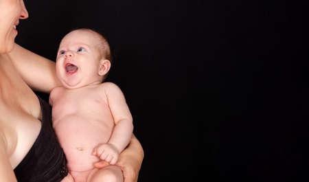 Laughing baby boy. Toddler in a yellow blanket. Cute little child boy smiling at camera. Adorable newborn baby lies on the hands his mother. Baby goods packaging template. Portrait of newborn babyの写真素材