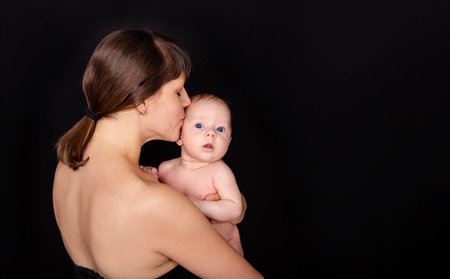 Happy mommy kissing baby boy. Mother kissing her adorable infant baby. Portrait of mother and her newborn baby together. Happy mother and baby hugging. Loving young mother hold little newborn.の写真素材