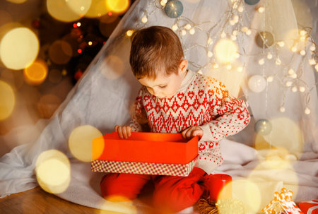 Surprised cute child opening a Christmas present. Little kid having fun near decorated tree indoors. Happy boy unwrapping his xmas gifts at home. Happy holidays and New Yea, Merry Christmas.の写真素材