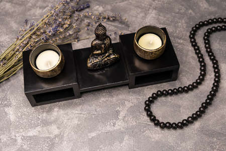 Statue of Buddha. Sculpture of buddha and a burning candle. Candlestick made of copper. Buddha statuette and wellness candle on grey background. Vintage bronze statuette with candlesticksの写真素材