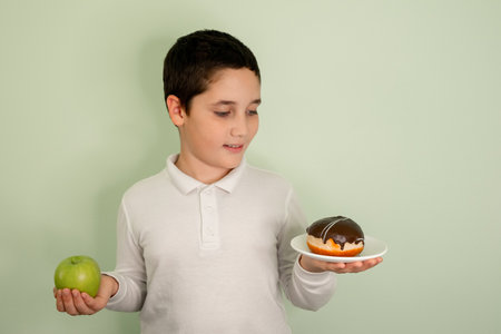 Kid choosing between apple and tasty sweets. Choice between tasty and healthy eating. Boy choosing junk food. Healthy versus unhealthy food. Teenager choosing between cookie or an apple.の写真素材