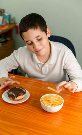 Kid eating chips having fun. Little child eats potato chips. Diet or healthy lifestyle concept. Happy boy eating a french fries. Painful preteen boy having abdominal pain, eating too much fried food.の写真素材