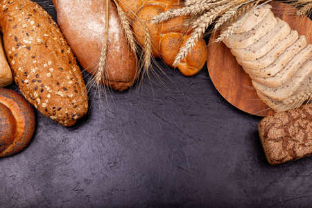 Assortment of fresh baked bread on dark background. Various tasty rolls and breads with grains close up on grey background. White and rye bread, buns with copy place. Composition with bread and rolls.の写真素材