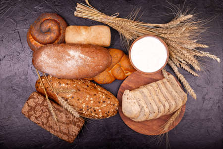 Top view of sliced wholegrain bread on dark ructic wooden background closeup. Various tasty breads with grains . White and rye bread, rolls and cream close-up . Composition with breads.の写真素材