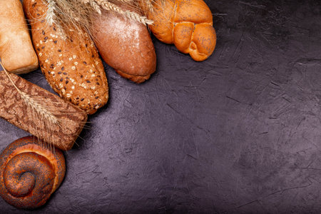 Various tasty rolls and breads with grains close up on grey background. Assortment of fresh baked bread on dark background. White and rye bread, buns with copy place. Composition with bread and rolls.の写真素材