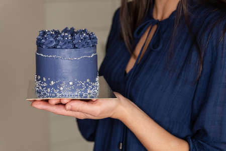 A woman prepares a cake with blue cream. Pastry chef holding a small cake. Womans hands holding...