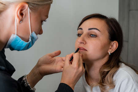 The makeup artist carefully draws the contour of the lips with a pencil to a beautiful girl Makeup...