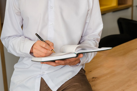 Business man in the workplace does records in a diary. Blank book page copy write a message. Young...