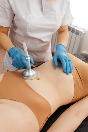 Beautician makes abdominal and waist massage to young woman. Lymphatic drainage massage. A professional cosmetologist performs an electromagnetic massage of the abdominal muscles on a woman patientの写真素材