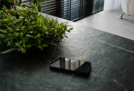 electronic devices. A single mobile phone on a wooden table in the office. Smart phone on table with bright morning window light streaming through. mobile phone on a table. Black cell phone on the tableの写真素材