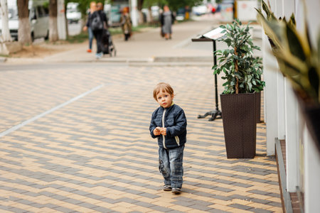 A cute boy is walking on the grass in a green summer park on a sunny afternoon. Little kid is examining plants in forest. A young boy walking on a summer day. Cheerful little boy in a spring gardenの写真素材