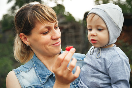Happy mother enjoying while feeding her son with strawberries. Mom and her son having snack time together. Mother giving son strawberries to taste. Beautiful mother feeding her baby boyの写真素材