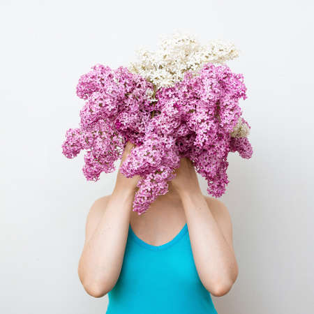 Shy girl in the blue dress hiding behind lilac flowers. Modesty conceptの写真素材