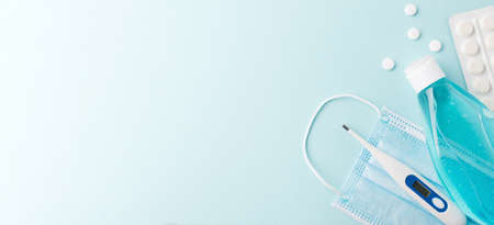 Blue medicine mask , pills, a safe electronic thermometer and a hand antiseptic gel on a blue...